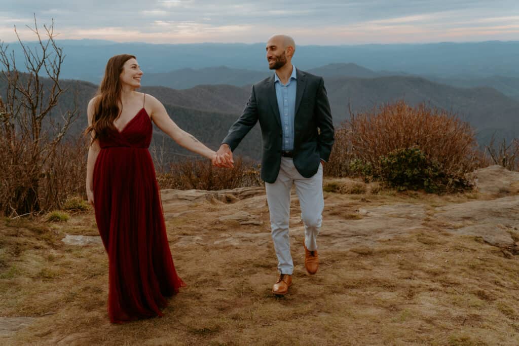 couple holding hands walking on top of mountain