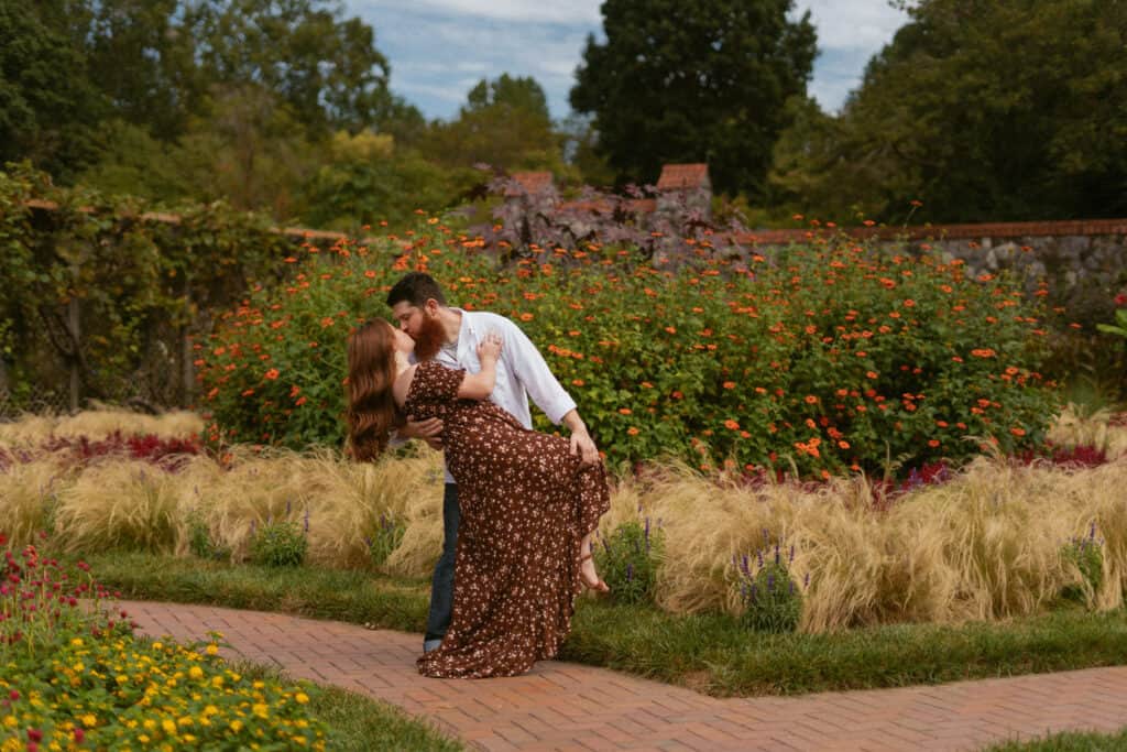 man dipping woman in front of flower garden for engagement photos at the biltmore
