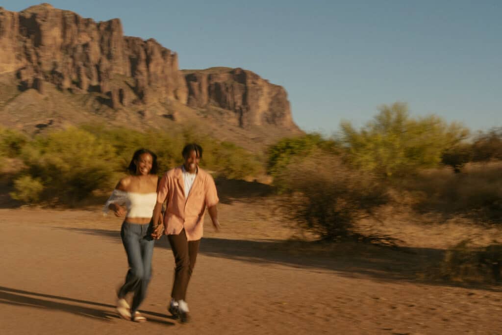 couple holding hands walking towards camera walking away from Superstition mountain