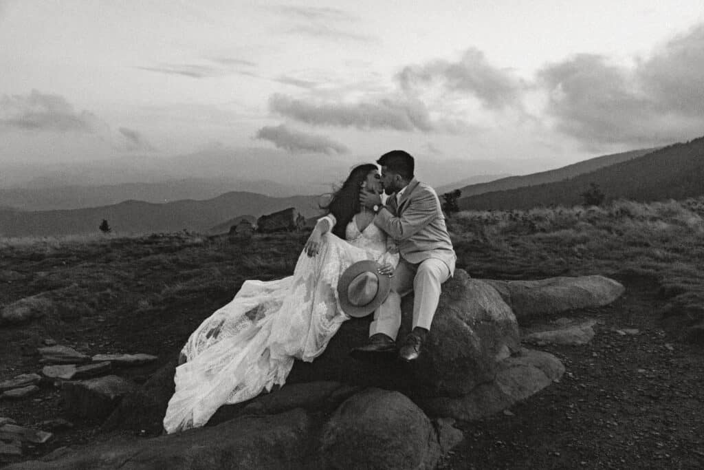 roan mountain elopement couple in wedding attire sitting on rock with panoramic mountain view