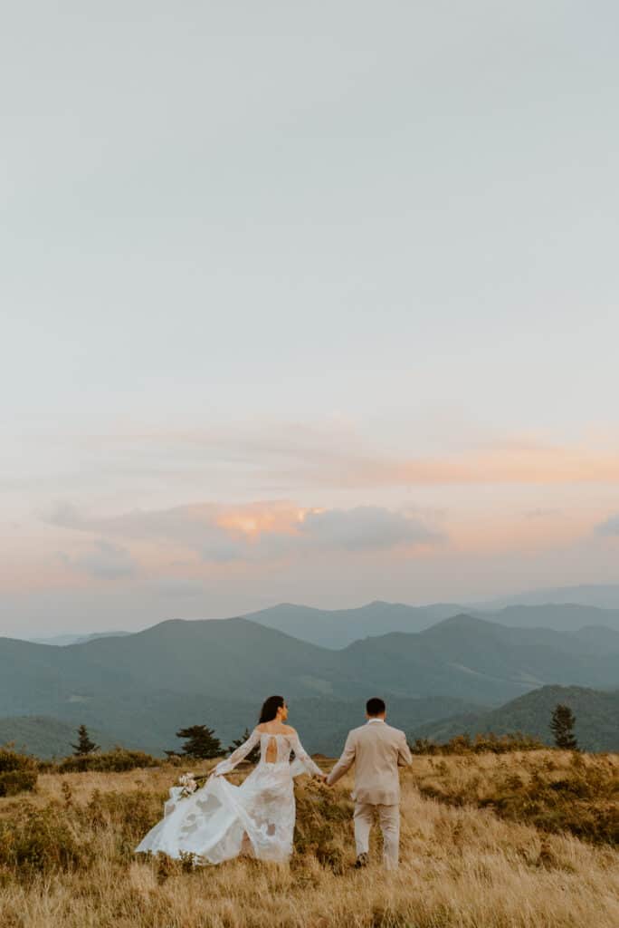 couple holding hands and walking away on top of mountain at sunset
