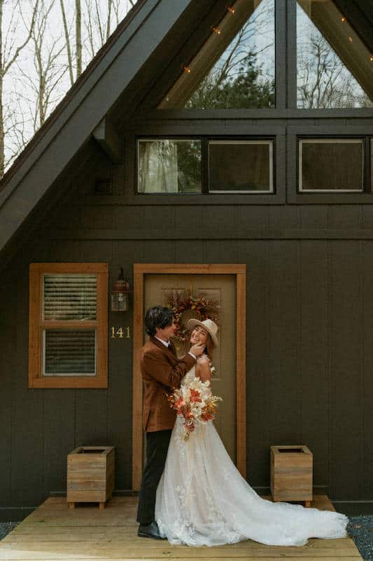 bride and groom posing in front of aframe cabin in the mountains close to asheville