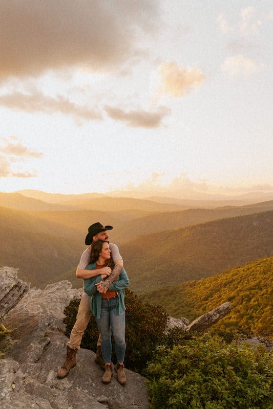 woman and man hugging on mountaintop at sunset in the mountains close to asheville